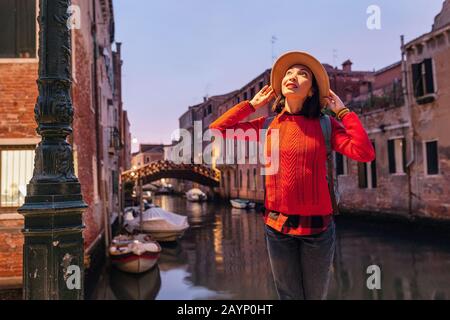 Junge, glückliche asiatische Reisende Frau am Pier eines schmalen Kanals und einer schmalen Straße in Venedig. Urlaub in Italien Konzept Stockfoto