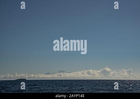 Weiße, flauschige Wolken in blauem Himmel über ruhigem Meer Stockfoto