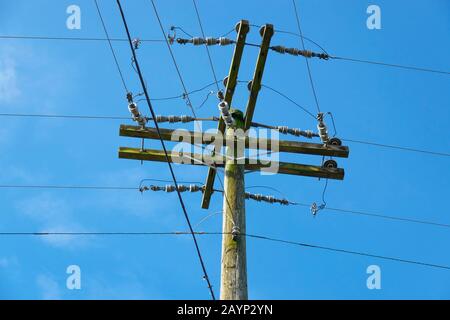 Ein Holz-Strompfosten mit Überkopfkabeln mit Isolatoren gegen einen blauen Himmel. Stockfoto