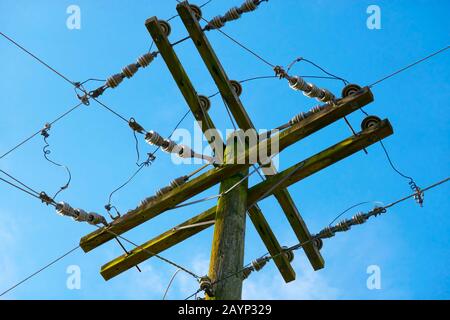 Nahaufnahme eines Holz-Versorgungsmastes mit Oberleitungen und Isolatoren gegen einen blauen Himmel. Stockfoto