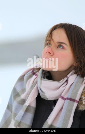 Wunderschönes junges Mädchen steht im Winter im Freien, eine Jacke und einen Schal im Hintergrund einer Winterlandschaft mit Schnee. Stockfoto