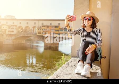Fröhliches junges Mädchen aus asien, das selfie in der Nähe der Brücke Ponte Vecchio nimmt