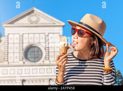 Junge, glückliche asiatische Touristin, die vor der Croce Basilica Kirche in Florenz Eis isst Stockfoto