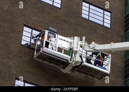 Ein Nahporträt aus zwei Fensterscheiben, mit einem Kran zu den oberen Fenstern des Gebäudes in einem großen Kasten zu gelangen, um bequem ihre Reinigungsaufgabe zu erledigen. Stockfoto