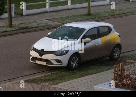 Ein Porträt eines sehr schmutzig weißen Autos, das an der Seite der Straße geparkt ist. Das Auto ist für eine Hälfte mit braunem Schlamm und Schmutz bedeckt. Stockfoto