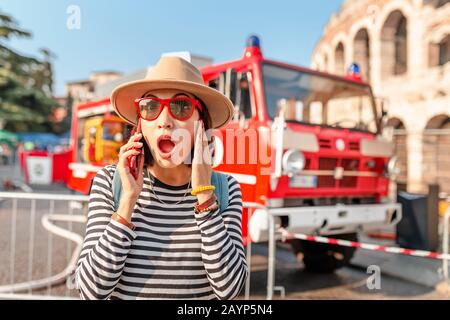 Frau mit Smartphone wählt Notruf oder 112-Nummer auf dem Bildschirm vor dem Hintergrund des Feuerwehrautos Stockfoto