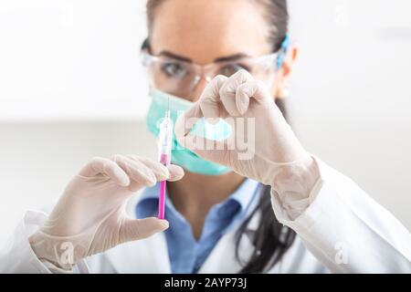 Ärztin arbeiten mit Nadel und ampulle von Medizin. Ein Wissenschaftler in sterilen Kleidung ist ein Impfstoff, der Droge. Stockfoto