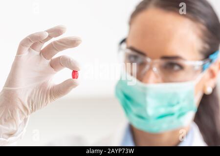Junge Wissenschaftlerin, die eine rote Pille hält - Nahaufnahme. Stockfoto