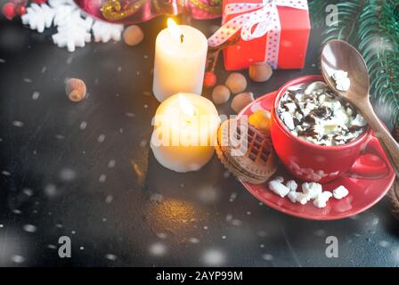 Heiße Schokolade in einem roten Becher mit Marshmallows, Keksen und Weihnachtsgeschenken im Hintergrund. Weihnachtsgetränk. Weihnachtsfeier Konzept. Stockfoto
