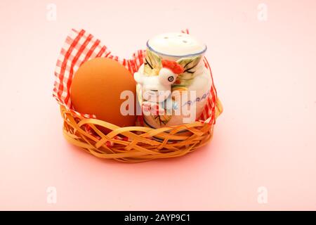 Weidenkorb mit Ostereiern und Salzkeller in Form eines Hähnchens auf rosa Hintergrund. osterkarte Stockfoto