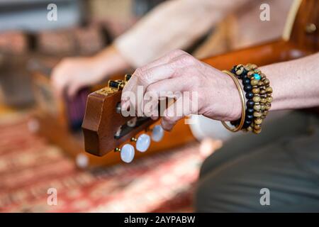 Nahaufnahme der weiblichen Hände, die klassische Gitarrensaiten zum Spielen heiliger Musik für die Meditation stimmen, während der Mann auf dem Bodenteppich sitzt Stockfoto