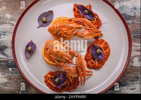 Gekochte Flusskrebse von oben auf einem Teller. Delikatesse mit Chili Pfeffersauce, Basilikum und Kapern. Gourmetküche Stockfoto