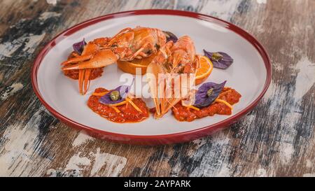 Lebensmittelbanner. Gekochte Flusskrebse. Delikatesse mit Chili Pfeffersauce, Orange, Zest, Basilikum und Kapern auf einem Teller. Haute Cuisine Stockfoto