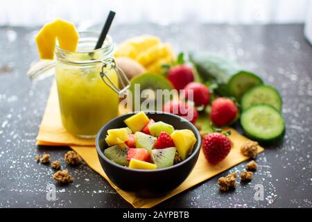 Gesundes Frühstück: Knusprige Müsli mit frischen Erdbeeren, Kiwi und Mango mit köstlichen grünen Smoothie im Mixbecher Stockfoto