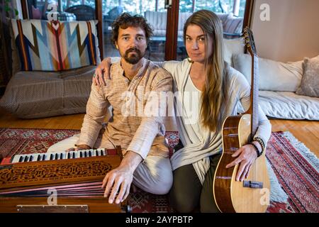 Junge schamanische Frau mit Hand auf der männlichen Schulter, die mit Musikinstrumenten wie klassischer Gitarre und Harmonium sitzt und heilige und kirtanische Musik spielt Stockfoto