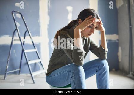 Portrait der frustrierten jungen Frau, die auf Farbe sitzt, kann durch Renovierungsprojekt, Kopierraum, verwüstet werden Stockfoto