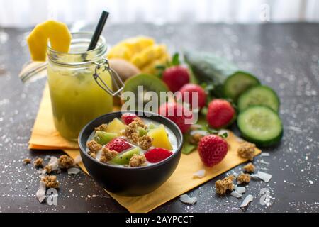 Gesundes Frühstück: Knusprige Müsli mit frischen Erdbeeren, Kiwi, Mango und Kokosflocken mit Joghurt, Serviert mit einem Smoothie in einem konservierenden Mixbecher Stockfoto