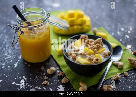 Köstliches Müsli mit frischen Mango-Stücken, Cashew-Nüssen und Joghurt mit einem Smoothie mit zerkleinerter Eiscreme Stockfoto