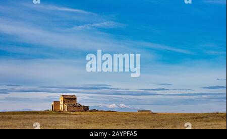 Naturlandschaft mit blauem Himmel und schneebedecktem Berghintergrund mit ländlichem Haus in der Herbstsaison und Agrarfeld auf einer Wiese Stockfoto