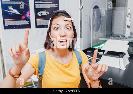 Lustige Frau mit digitalem Headwear Equipment Sensor, der an ihr Ohr angeschlossen ist und Gehirnimpulse liest. Zukünftiges Technologiekonzept Stockfoto