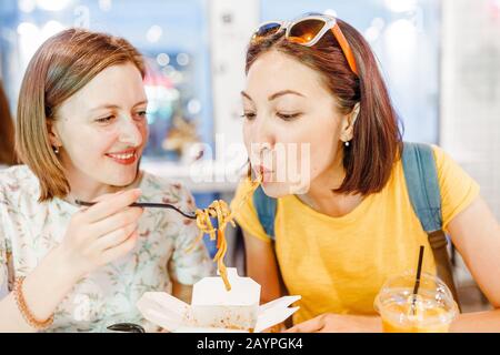 Zwei Freunde Frau, die Wok Nudeln im Café isst Stockfoto