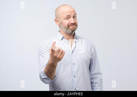 Ein gutaussehender reifer Mann, der Geste zeigt, kommt hierher. Studio gedreht Stockfoto