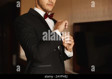 Gutaussehende Geschäftsleute in Tuxedo und bowtie, die Manschetten an einer Manschette mit weißem Hemd befestigen, beschnitten in der Nähe. Halbgesicht Porträt eines stylischen Mannes im Anzug Stockfoto