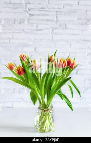 Wunderschöner roter und gelber Blumenstrauß aus Tulpenblumen auf weißem Regal vor weißer Ziegelwand. Kopierbereich. Horizontale Ausrichtung. Stockfoto