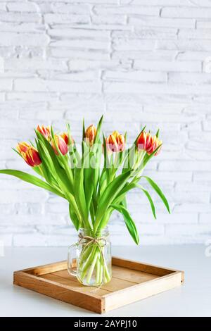 Wunderschöner roter und gelber Blumenstrauß aus Tulpenblumen auf weißem Regal vor weißer Ziegelwand. Kopierbereich. Horizontale Ausrichtung. Stockfoto