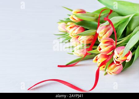 Wunderschöner roter und gelber Blumenstrauß aus Tulpenblumen auf weißem Regal vor weißer Ziegelwand. Kopierbereich. Stockfoto