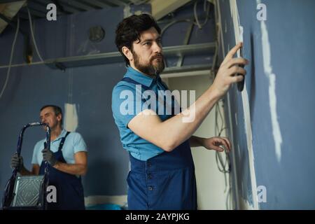 Seitenansicht Porträt des bärtigen Mannes, der an einer trockenen Wand arbeitet, während das Haus renoviert wird, Kopierraum Stockfoto