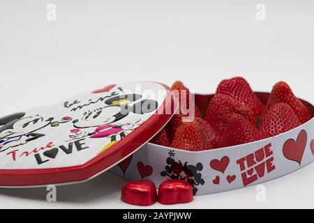 valentinsgeschenk in Herzform mit Erdbeeren geöffnet und Schokoladenbonbons mit Deckel eingewickelt Stockfoto