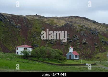 Ein Bauernhof und eine Kirche sitzen in einem Schlackenkrater Ytri Raudamelskula auf der Halbinsel Snaefellsnes im Westen Islands. Stockfoto