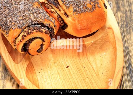 Unedle frische Brötchen mit Mohnsamen liegen auf Holztablett auf Holzoberfläche in der Nähe, Kopierraum. Stockfoto