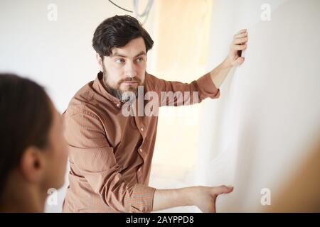 Taille oben Porträt des bärtigen Mannes, der Tapete an der Wand hält, während das Haus, der Kopierraum, neu dekoriert wird Stockfoto