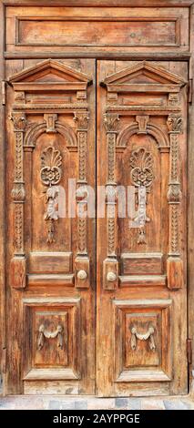 Alte Holzeingangstüren mit geschnitzten Elementen, die an der Fassade mit einem geschnitzten symmetrischen Muster von oben nach unten gerahmt sind. Stockfoto