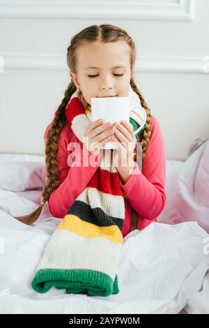 Krankes Kind im Schal mit einer Tasse heißem Getränk im Bett Stockfoto
