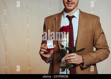 Teilansicht des eleganten Herrenhalters mit Hochzeitsring und roter Rose im Restaurant Stockfoto