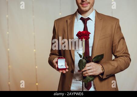 Teilansicht des eleganten Herrenhalters mit Hochzeitsring und roter Rose im Restaurant Stockfoto