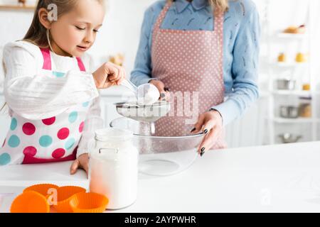 3/4-Ansicht der Mutter, die Sieb hält, und der niedlichen Tochter, die Mehl sietet Stockfoto