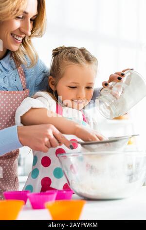 Selektiver Fokus von schöner Mutter und süßer Tochter, die Mehl durch ein Sieb in eine Schüssel sieben Stockfoto