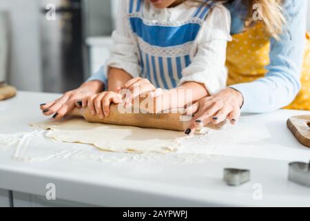 3/4-Ansicht von Mutter und Tochter, die Teig auf dem Tisch rollen Stockfoto