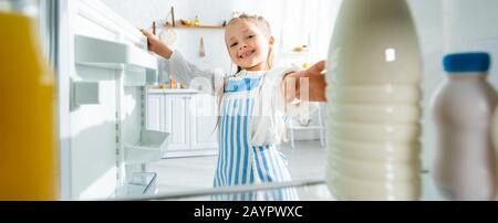 Panoramaaufnahme des lächelnden Kindes, das Flasche mit Milch aus dem Kühlschrank nimmt Stockfoto