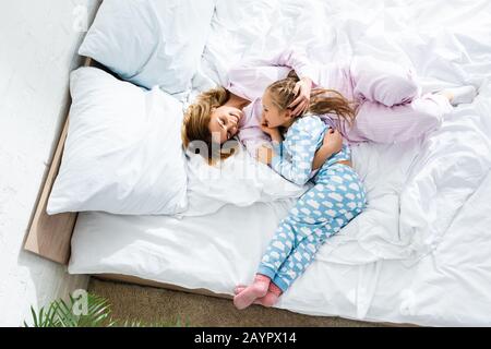 Draufsicht über lächelnde Mutter, die Tochter umarmt und im Bett liegt Stockfoto