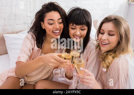 Attraktive, fröhliche multikulturelle Mädchen, die auf der Junggesellen-Party mit einer Gläser Champagner einklinken Stockfoto