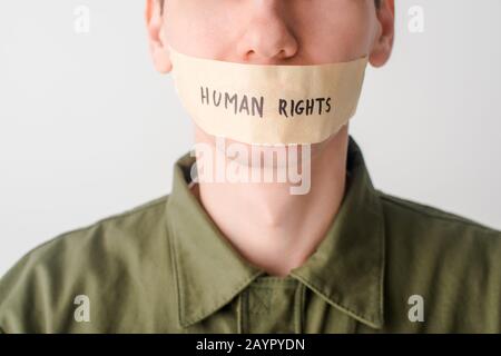 3/4-Ansicht des Menschen mit Klebeband am Mund mit Menschenrechts-Schriftzug auf weiß isoliert Stockfoto