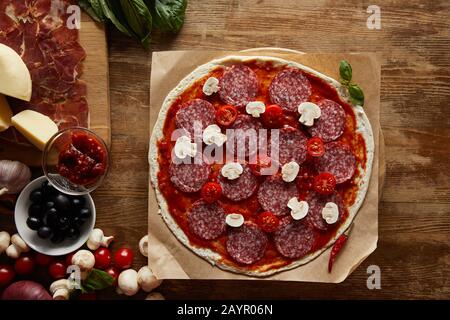 Blick auf Pizza mit Salami, Pilzen und Tomatensauce auf Holzgrund Stockfoto