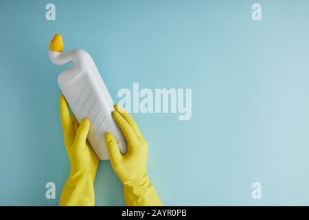 3/4-Ansicht der Haushälterin in gelben Gummihandschuhen, die Flasche mit toilettenreiniger auf blau halten Stockfoto