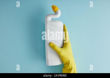 3/4-Ansicht der Haushälterin in Gummihandschuhflasche mit toilettenreiniger auf blau Stockfoto