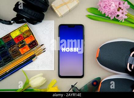 Logo der HOBBI-App auf dem Smartphone und Teile, die beliebte Hobbys darstellen. Facebook hat vor kurzem die App Hobbi veröffentlicht. Flaches Laienfoto. Stockfoto